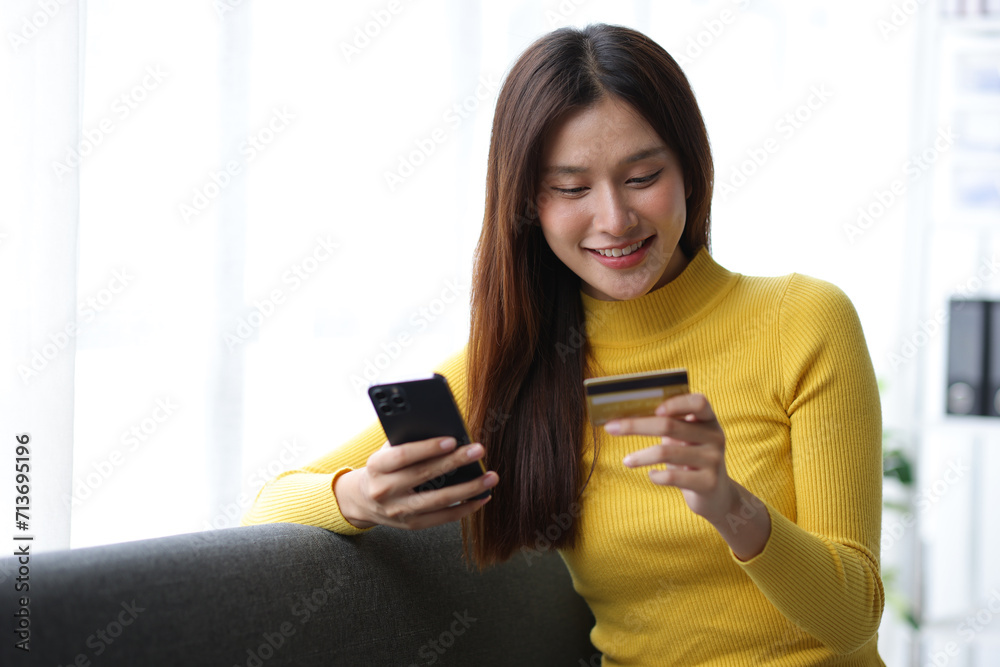 Beautiful Asian woman on sofa at home using credit card doing online shopping from home using smartphone. Beautiful Asian woman on sofa at home using credit card doing online shopping from home using smartphone.