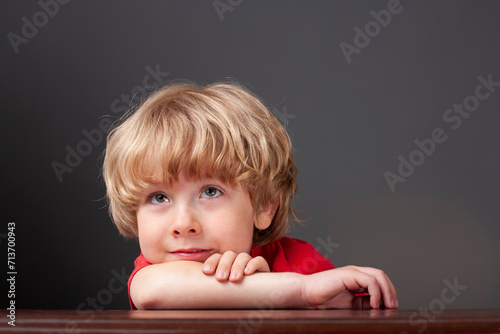 Fotografi Young smiling boy looking up thinking at a table