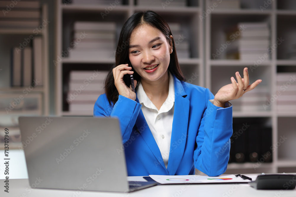Businesswoman working overtime in the home office is using mobile phone to send messages and chat with colleagues, and analyzing monthly work schedule.