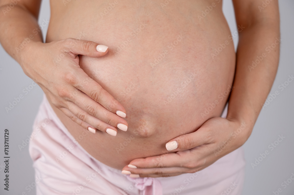 Close-up of pregnant woman's belly in third trimester on white background. 