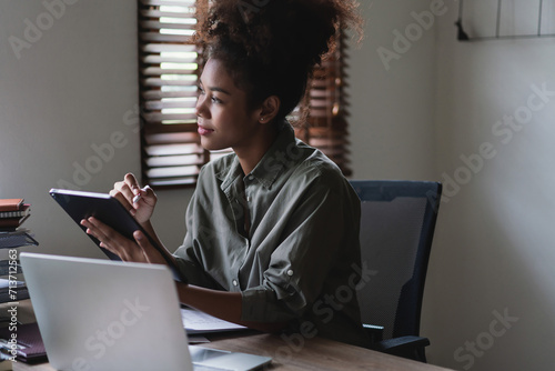 African american businesswoman writing finance data on tablet and working on laptop in workplace photo