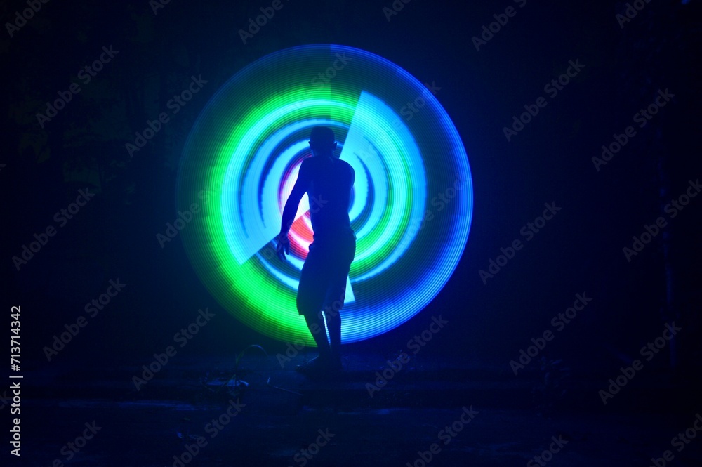 One person standing alone against a Colourful circle light painting as the backdrop	