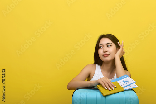 Beautiful young Asian brunette with plane tickets in her hands straightens her hair with her hand, looks away. Young woman passenger on a plane flight waiting for departure on a yellow background