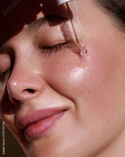 Serum. Moisturising and nourishing.  Close up beauty portrait of  beautiful woman with glowing skin is applying a vitamin c skincare product with a pipette dropper.