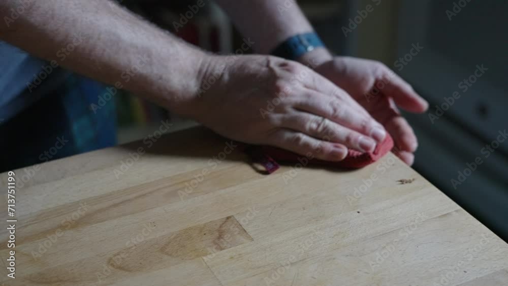 Cleaning crumbs off a butcher's block counter with an orange dish cloth, in a modern kitchen in natural daylight Cleaning crumbs off a butcher's block counter with an orange dish cloth, in a modern kitchen in natural daylight