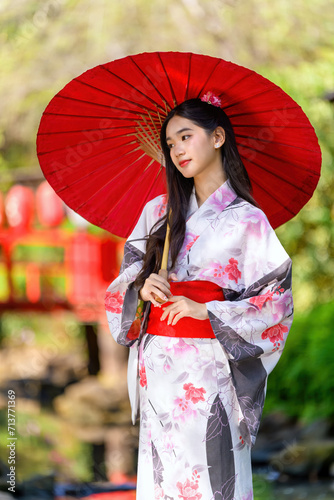 Photography A young woman wearing a Japanese traditional kimono or yukata holding an umbrella is happy and cheerful in the park