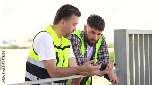 two Tired Engineer Take A Break after work talking and watching mobile phone to rest on rooftop . slacker play social media in work time . slack off photo