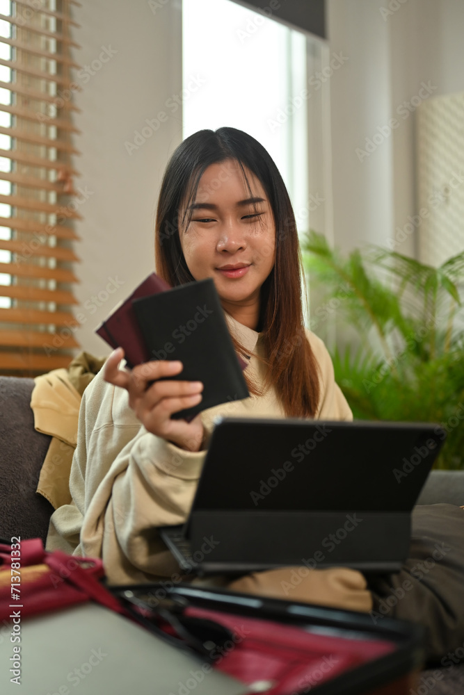 Pleasant young woman holding passport and booking flight tickets on digital tablet Pleasant young woman holding passport and booking flight tickets on digital tablet