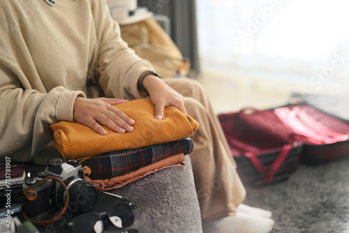 Cropped shot young woman sitting on couch packing suitcase for vacations trip.