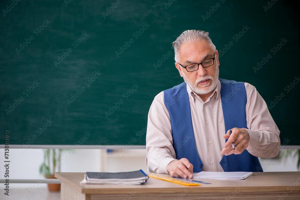 Old male teacher in front of green board Old male teacher in front of green board