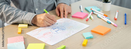 Skilled businessman brainstorms marketing ideas using mind maps. Successful male startup leader drafts financial plan on table with sticky notes scatter around. Closeup. Focus on hand.Variegated.