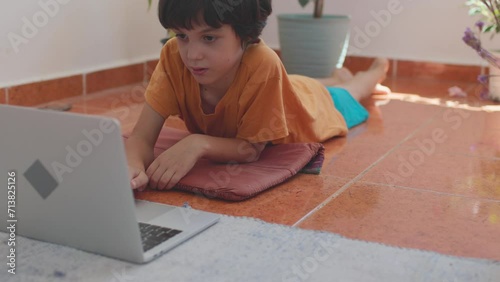 Happy boy using laptop while lying on the floor in his room. video call for e-learning, education or virtual classroom at home. online learning at home photo