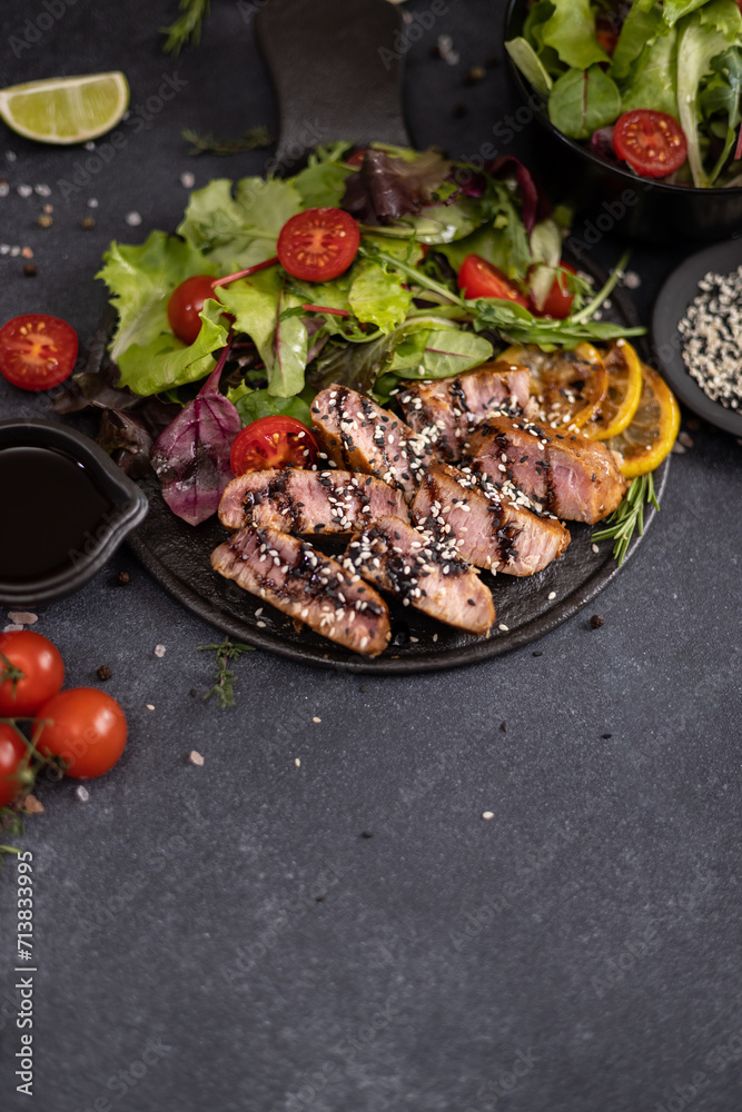 sliced grilled Organic Tuna Steak on black ceramic serving dish with salad on a table