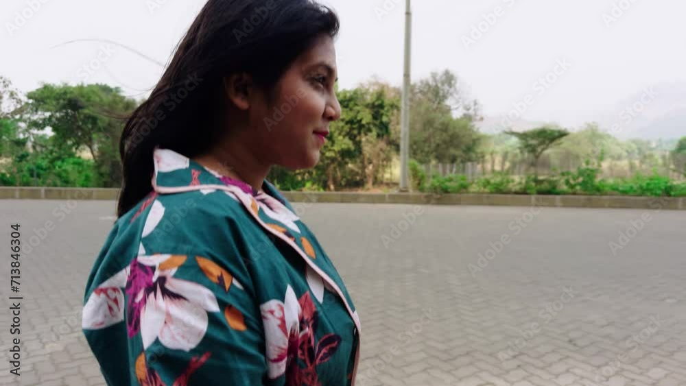Smiling woman walking on street outdoors in a floral dress looking over her shoulder with a natural background Smiling woman walking on street outdoors in a floral dress looking over her shoulder with a natural background