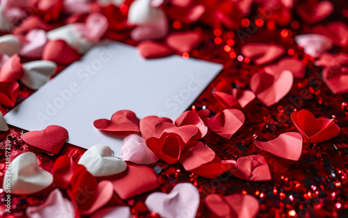 Elegant red and pink hearts scattered around a blank white card on a crimson background, symbolizing love, Valentine's Day, and romantic celebrations