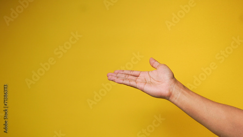 A man's hand shows a palm up gesture on a yellow orange background
