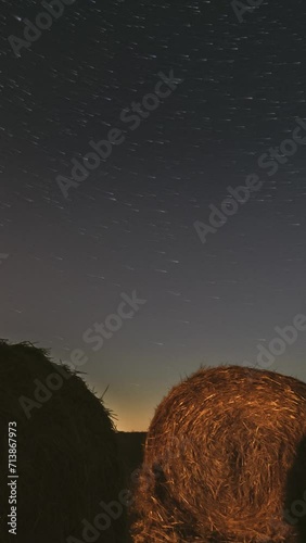 Comet Neowise C 2020 F3 In Night Starry Sky Above Haystacks In Summer Agricultural Field. Night Stars Above Rural Landscape With Hay Bales After Harvest. Agricultural Concept. 4K Timelapse. photo