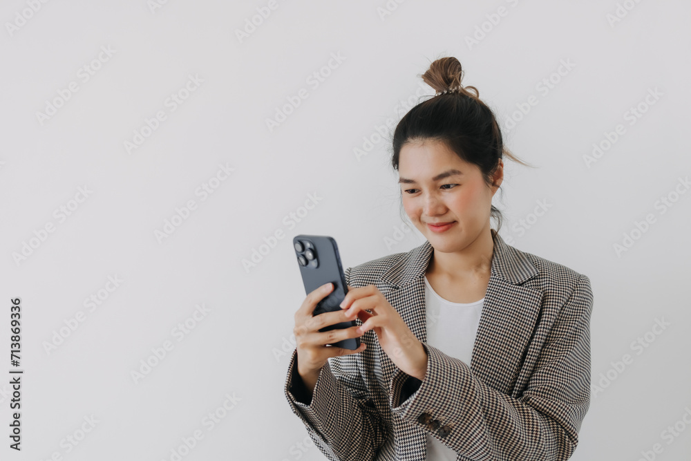 Asian Thai woman happy using mobile phone, looking and holding smartphone, wear blazer suit smart clothes, standing isolated over white background wall. Asian Thai woman happy using mobile phone, looking and holding smartphone, wear blazer suit smart clothes, standing isolated over white background wall.