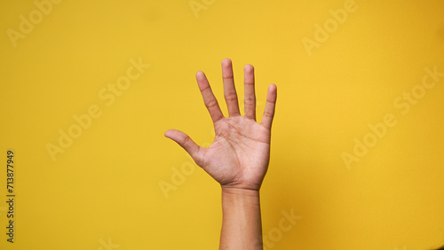 Man's hand lifting up and waving saying hi or asking permission on a yellow background