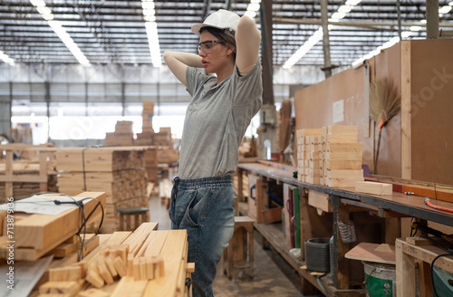 Confident female worker working in hardwood warehouse of wooden furniture factory checking stock. Busy skilled inspector in uniform hardhat examining plank pallet material for production facility.