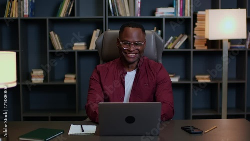 Medium shot of a black man working online at a laptop at a table at home, young man working remotely online at a laptop at home, remote work online at a laptop at home, zoom call, skype, meeting.