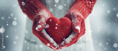 Hands of a woman wearing knit mittens with a snowy heart on a snowy background