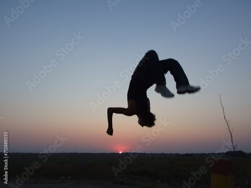 Silhouette of a guy doing a backflip in parkour style at sunset