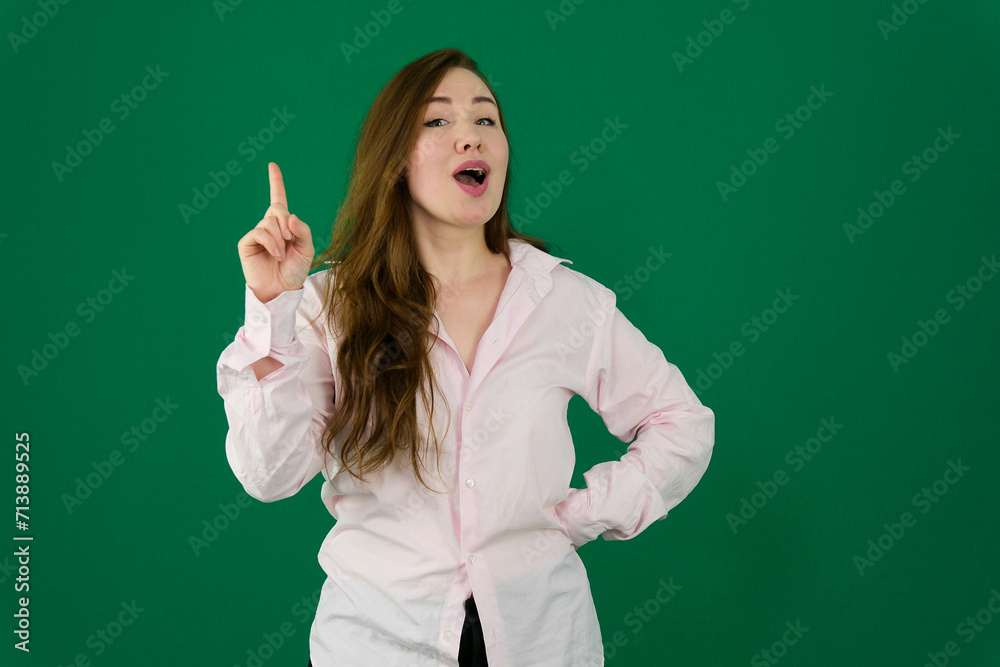 Surprised young woman looking up while pointing her finger against a green background. High quality photo Surprised young woman looking up while pointing her finger against a green background. High quality photo