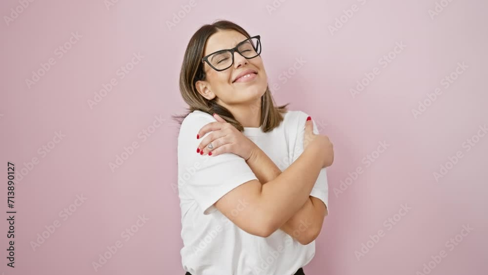 Confident and happy young hispanic woman embracing self love, wearing glasses, smiling radiantly, hugging herself against isolated pink background Confident and happy young hispanic woman embracing self love, wearing glasses, smiling radiantly, hugging herself against isolated pink background