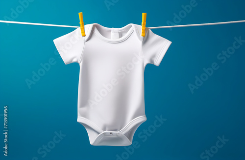White baby onesie drying and hanging on a rope with yellow pegs, blue background