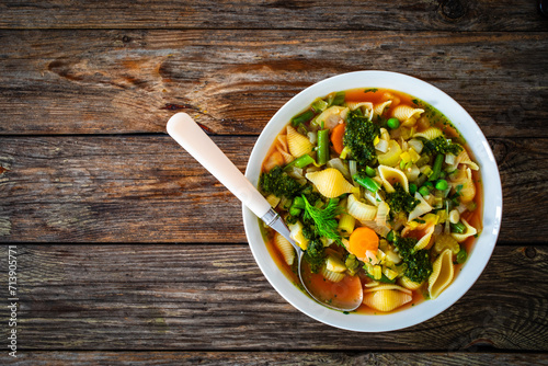 Pistou soup Nice - broth with basil pesto, noodles and vegetables on wooden background in white bowl photo