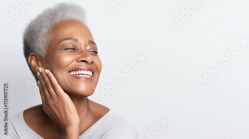 Lady advertising anti age face skin and body care treatment cosmetics isolated on gray background. Senior woman touching, massaging beautiful face, smiling. Elderly female with grey hair and soft skin photo