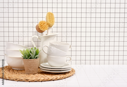An eco brushed jug, clean plates and mugs stand on a wicker hot food stand. Copy space for text.