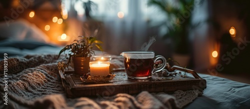 cup of tea with burning candle on wooden tray on bed in bedroom in evening. Creative Banner. Copyspace image