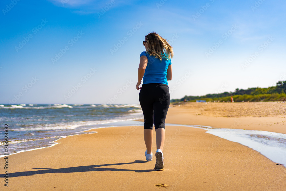 Mid adult beautiful woman running on sunny beach 