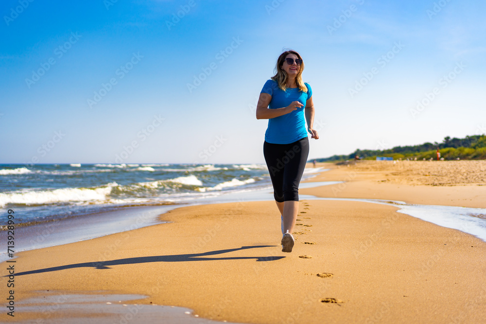 Mid adult beautiful woman running on sunny beach 