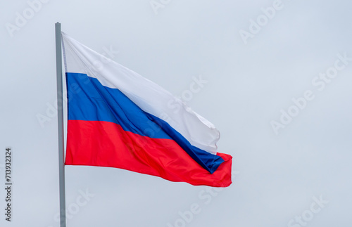 The white-blue-red flag of the Russian Federation is flying in the wind against a cloudy sky.