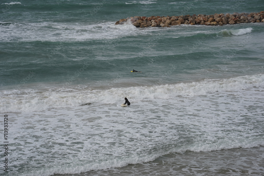 Strong currents and waves in the sea and surfers. Waves successfully crash into the stone breakwater.