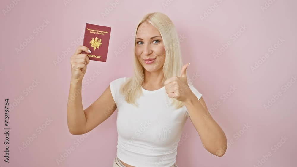 Cheery, attractive young blonde woman flashing a confident smile and 'okay' hand sign, asserting her approval, holding france's passport over isolated pink background. Cheery, attractive young blonde woman flashing a confident smile and 'okay' hand sign, asserting her approval, holding france's passport over isolated pink background.