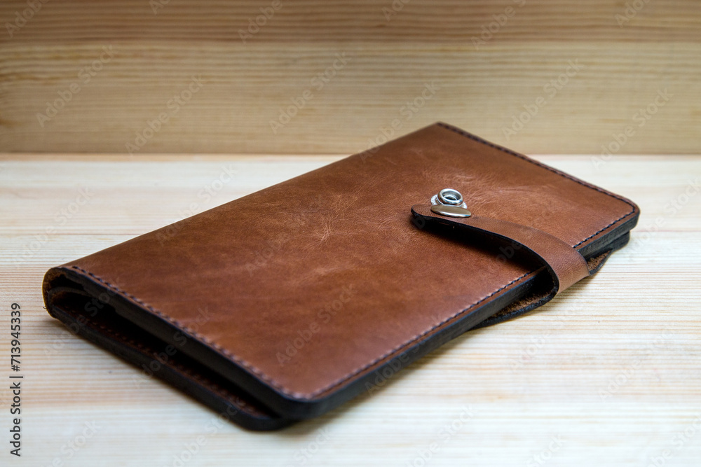 Men's wallet made of rough brown leather on light wood background. A stylish accessory for men, made in a classic design. Men's wallet made of rough brown leather on light wood background. A stylish accessory for men, made in a classic design.