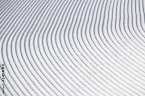 Curve lines in groomed winter snow surface on white ski slope abstract texture background