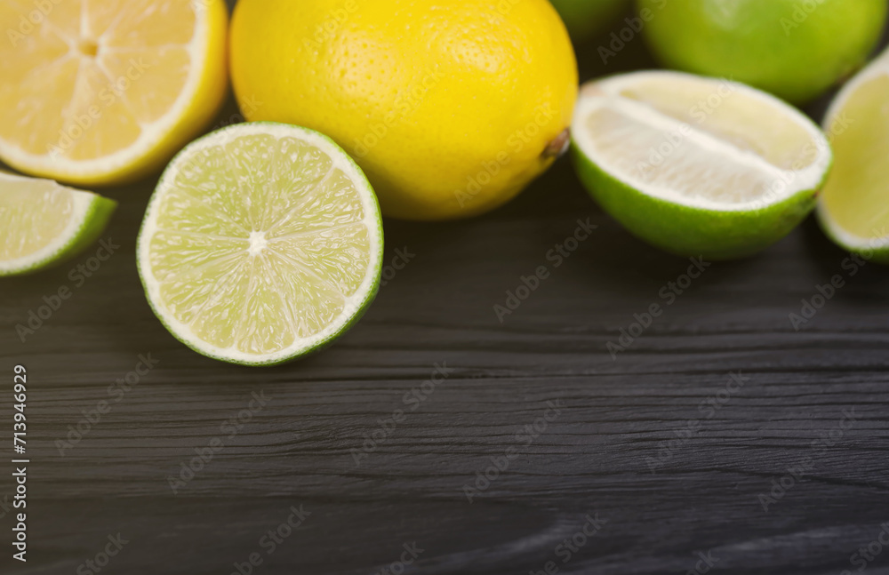 Many halves and slices of yellow lemon and green lime on black wooden table. Fresh fruits on kitchen top with copy space for your text