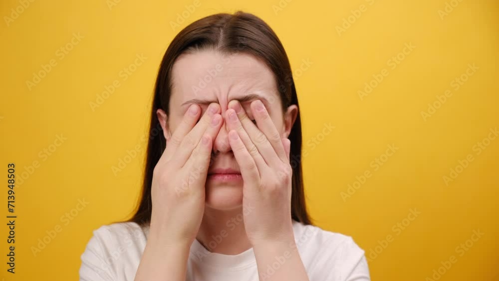 Close up portrait of young woman suffering from eyes pain, isolated on yellow background wall. Cause of pain include contact lens problem, conjunctivitis, foreign object, dry eye syndrome or allergy Close up portrait of young woman suffering from eyes pain, isolated on yellow background wall. Cause of pain include contact lens problem, conjunctivitis, foreign object, dry eye syndrome or allergy
