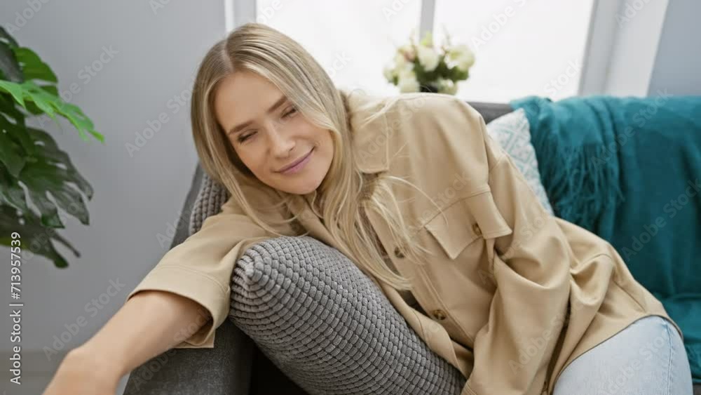 Confident young blonde enjoying relaxation, smiling while sitting comfortably on cozy sofa at home Confident young blonde enjoying relaxation, smiling while sitting comfortably on cozy sofa at home