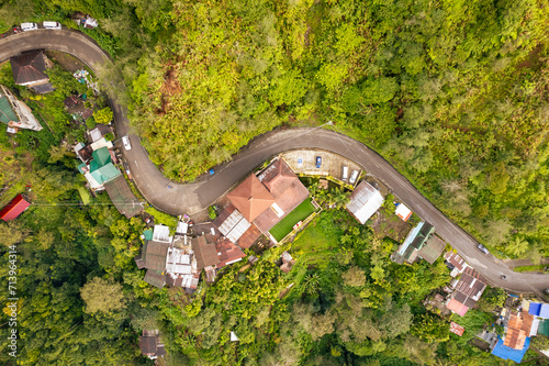 Top-down drone shot of a highway surrounded by houses cutting through the forest. At the town of Banaue, in the province of Ifugao, Philippines.