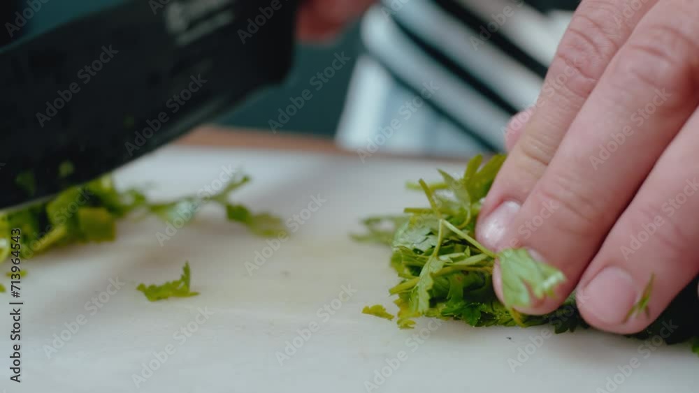 hands finely chopping parsley on white cutting board with a knife. The wooden surface and striped apron provide This image is suitable for stock sites, highlighting culinary skills hands finely chopping parsley on white cutting board with a knife. The wooden surface and striped apron provide This image is suitable for stock sites, highlighting culinary skills