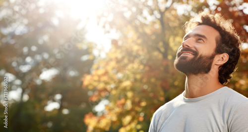smiling young man with closed eyes in park on sunny autumn day