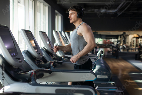 Muscular man athlete in wireless headphones running on treadmill in gym, listening music during workout, enjoying cardio training