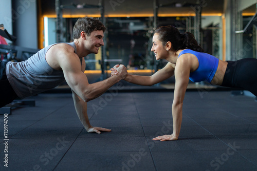 Happy young athletic couple exercising push-ups or plank while holding hands during cross training in gym, side view