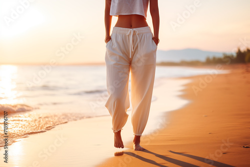 Woman wearing white clothes walking along a beach during sunset